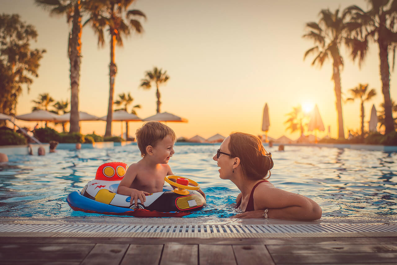 Mother and son playing in swimming pool at sunset